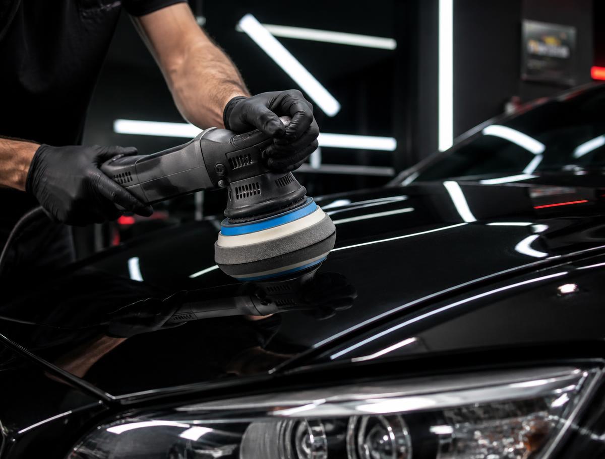 Detailer machine-polishing a glossy black car hood